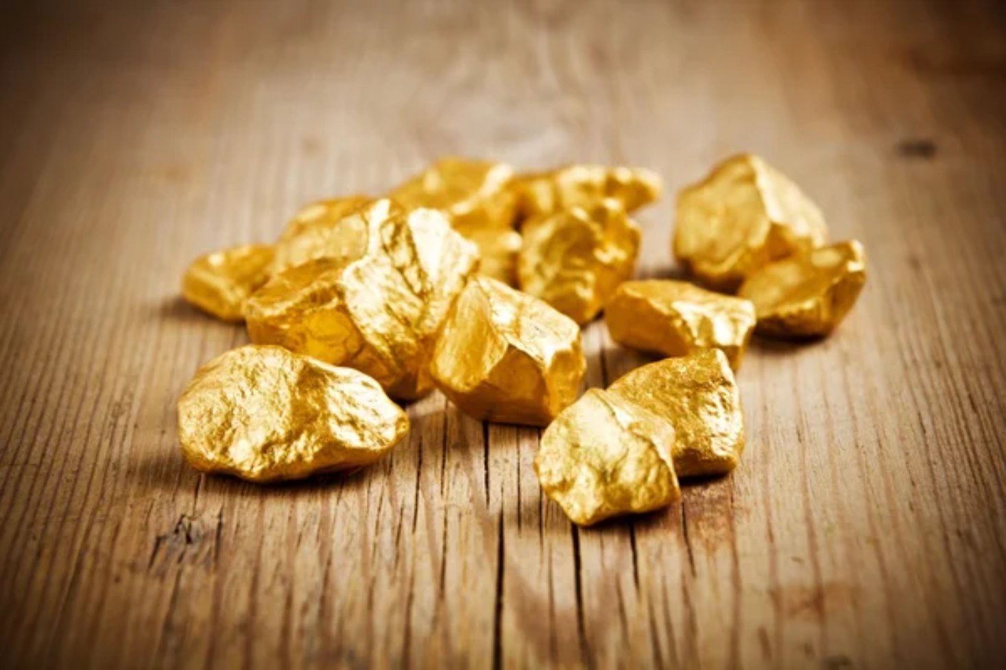 Close up of a gold bar and gold coins with financial trends indicated on sheet beneath gold.